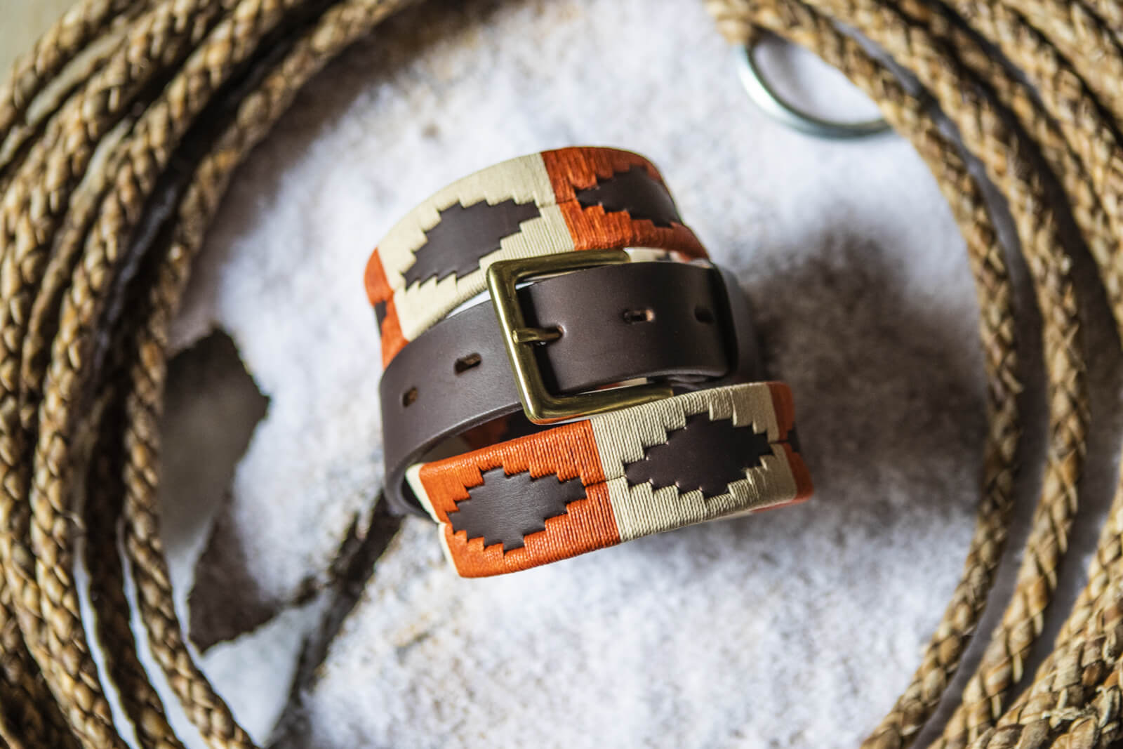 A brown leather belt with a burnt orange and khaki woven geometric pattern and solid brass buckle.