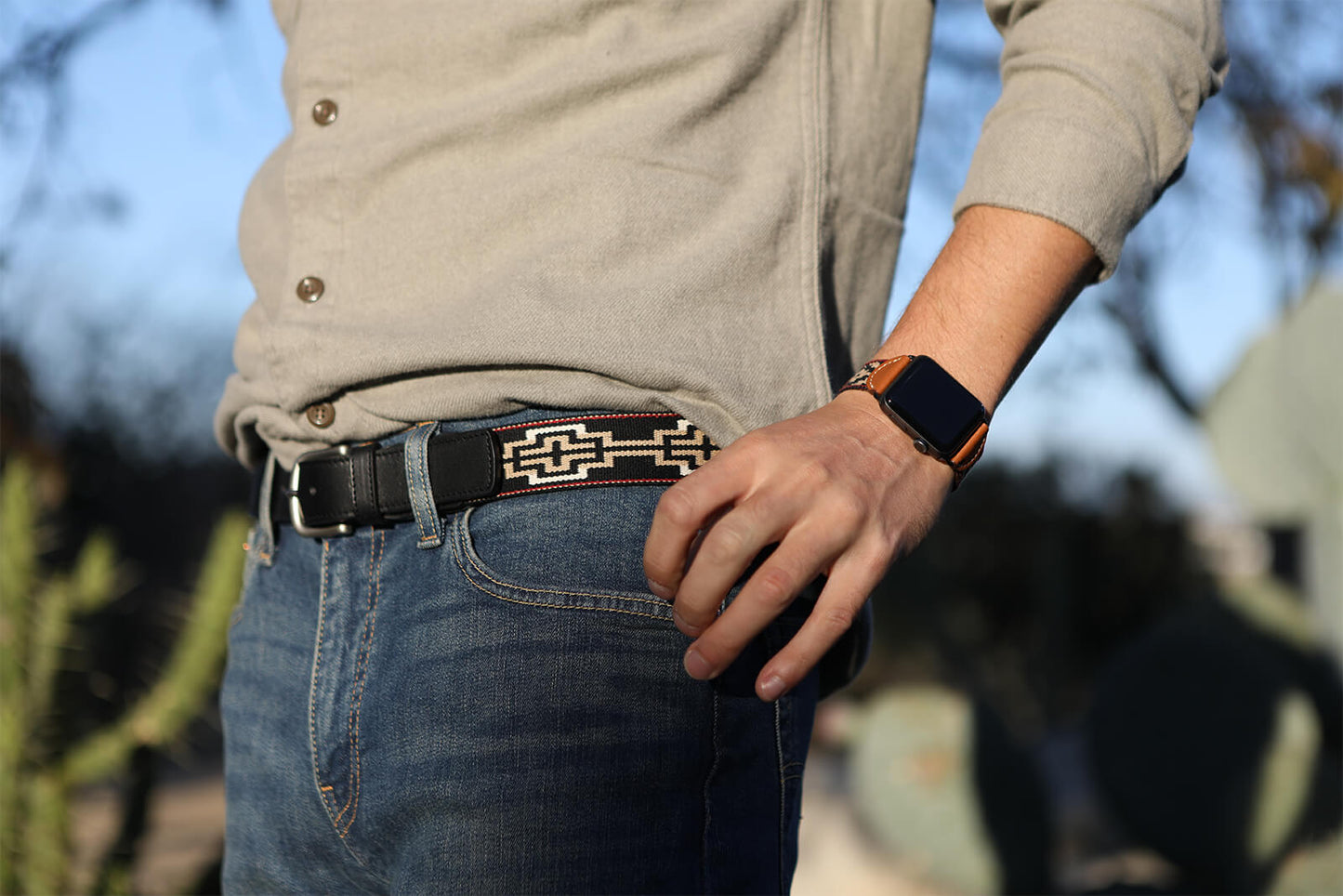 A black leather belt with a black, white, khaki & red woven geometric pattern and nickel-matte solide brass buckle.