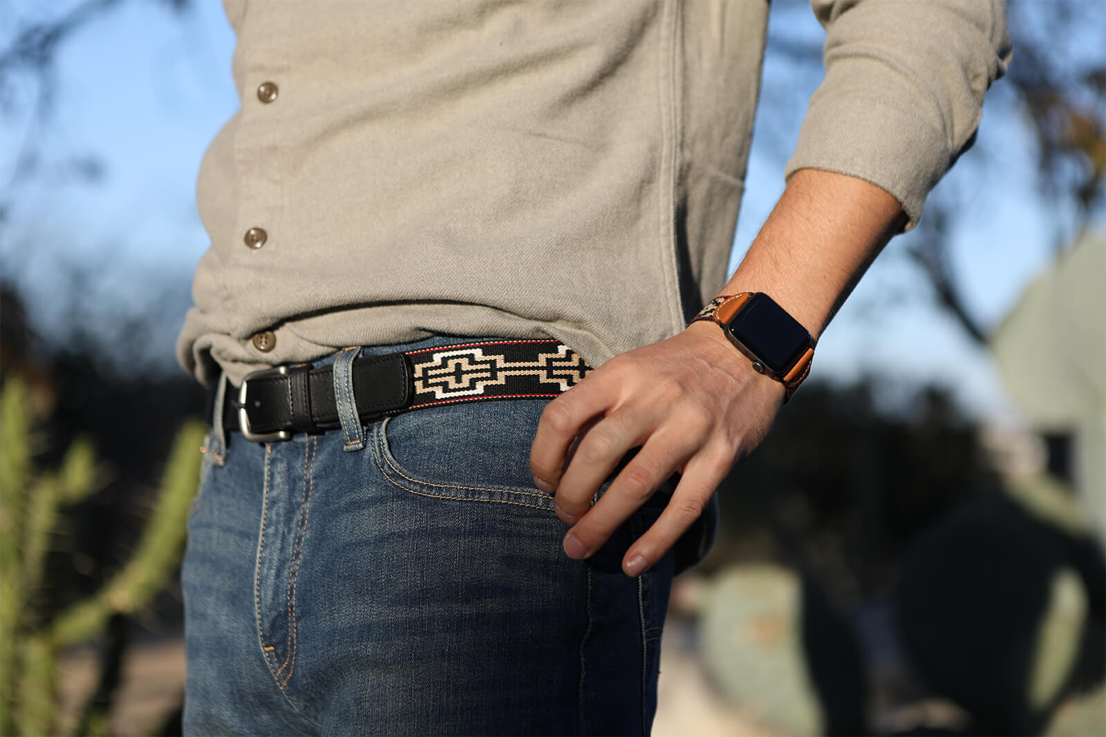 A black leather belt with a black, white, khaki & red woven geometric pattern and nickel-matte solide brass buckle.