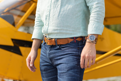A brown leather belt with a red and deep navy woven geometric pattern and solid brass buckle.