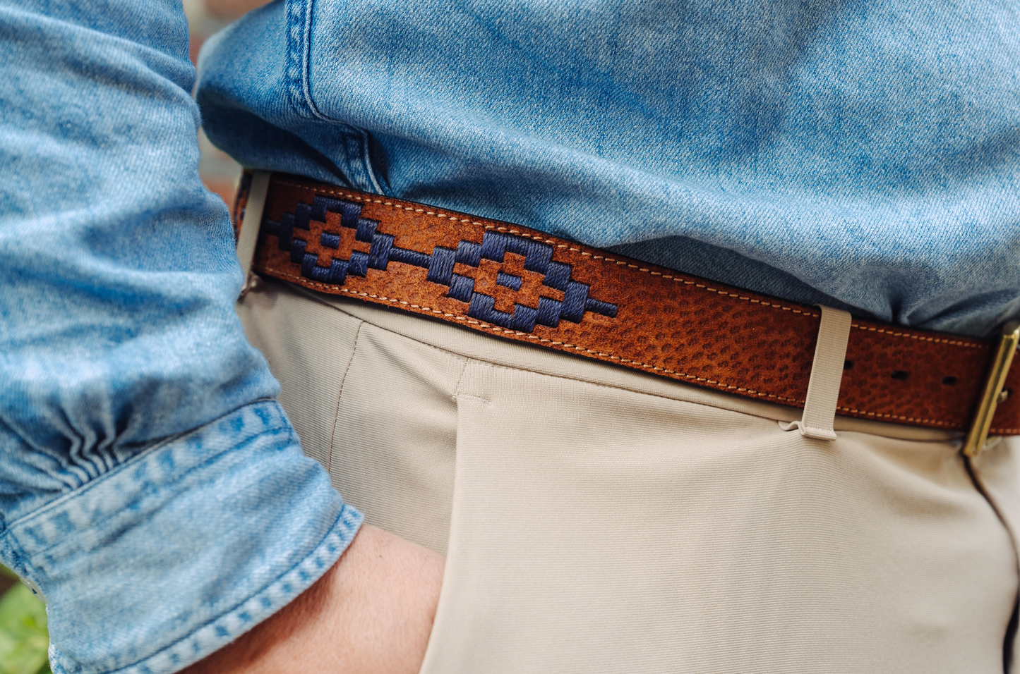 A tan leather belt with a navy woven geometric pattern and solid brass buckle.