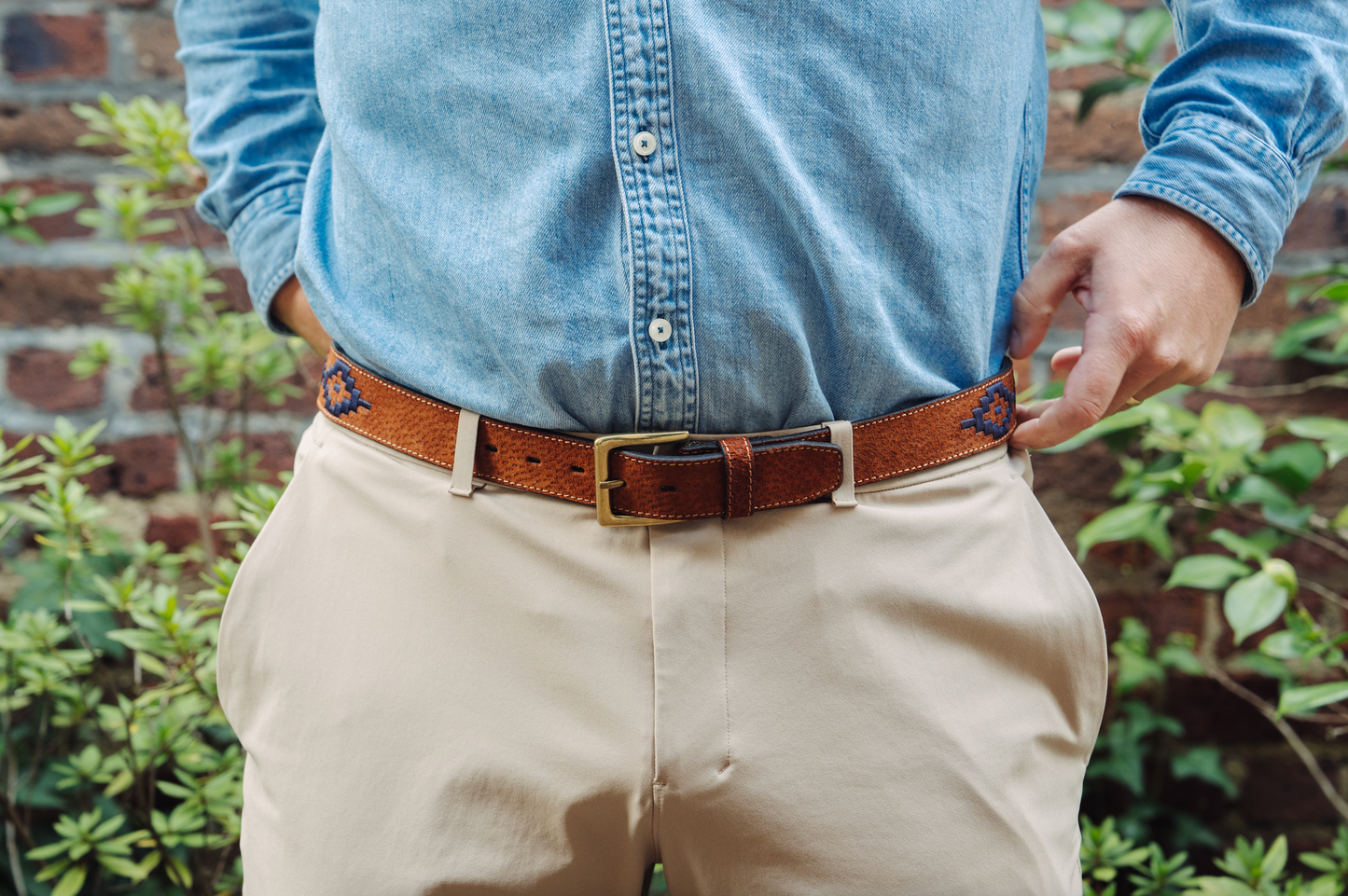 A tan leather belt with a navy woven geometric pattern and solid brass buckle.