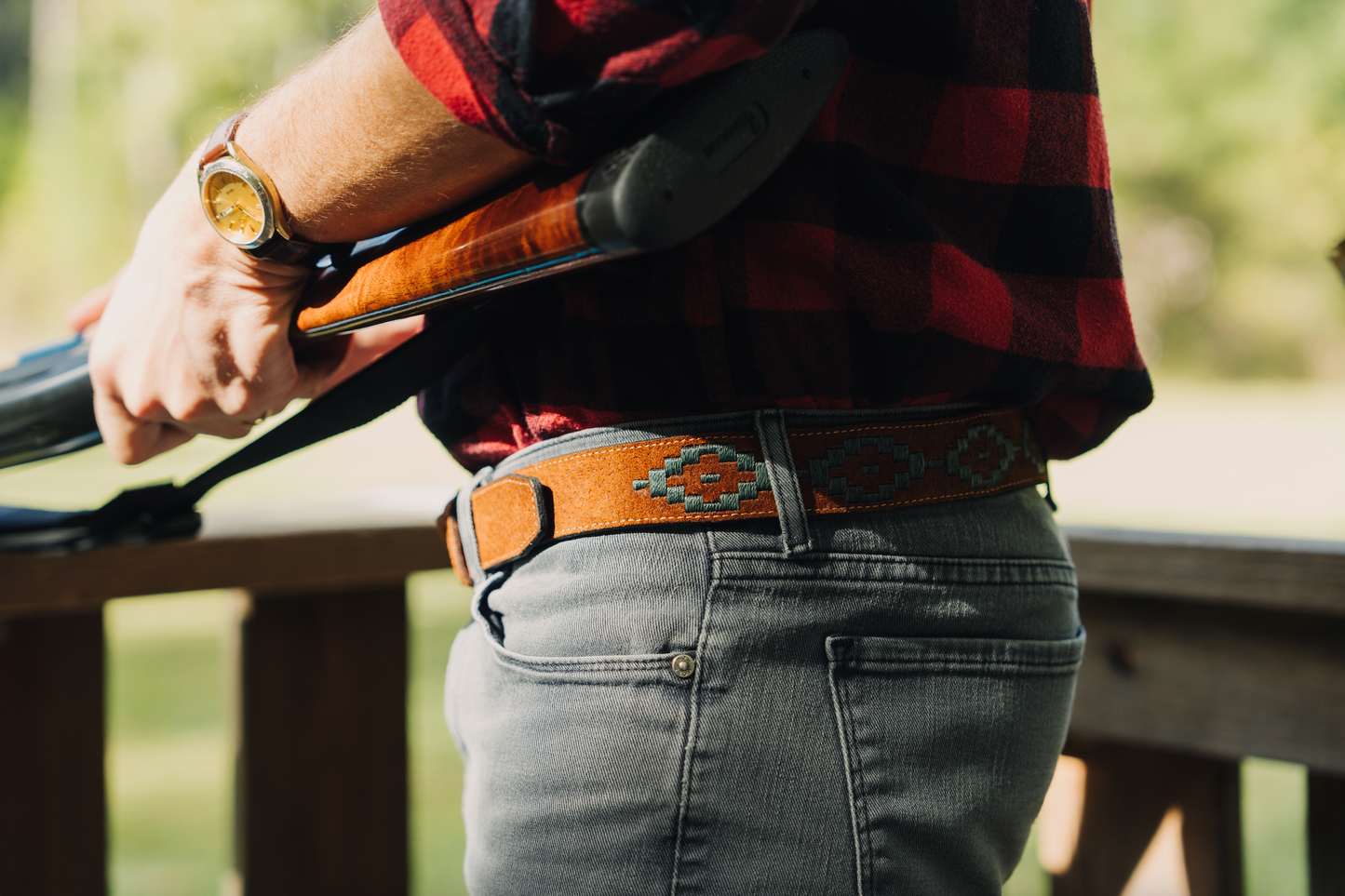 A brown leather belt with a hunter green woven geometric pattern and solid brass buckle.