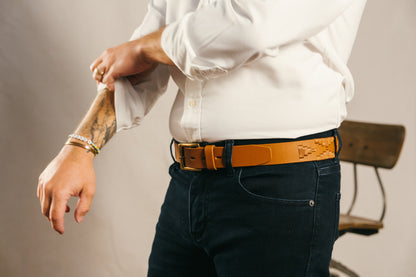 A tan leather belt with a tan woven geometric pattern and solid brass buckle.