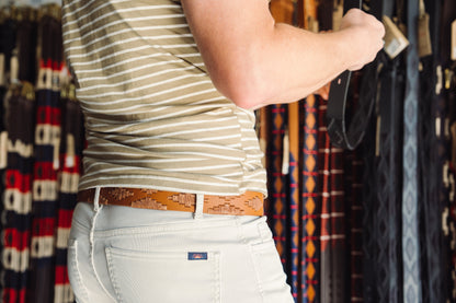 A tan leather belt with a tan woven geometric pattern and solid brass buckle.