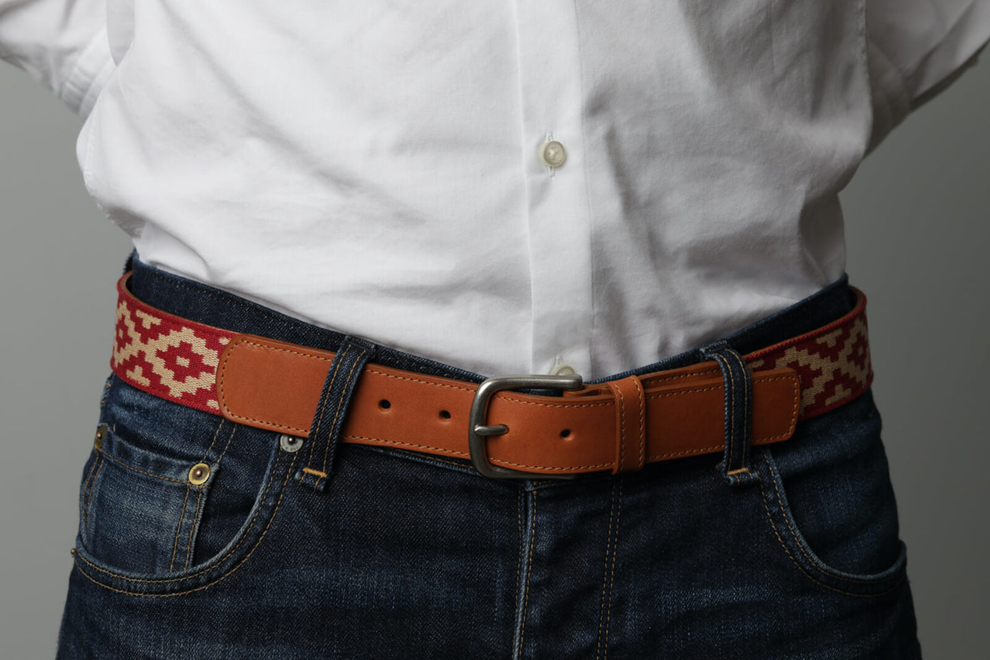 A brown leather belt with a red and beige woven geometric pattern and solid brass buckle.