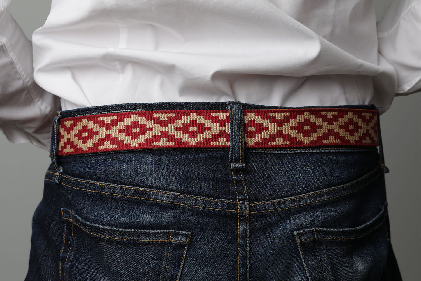 A brown leather belt with a red and beige woven geometric pattern and solid brass buckle.