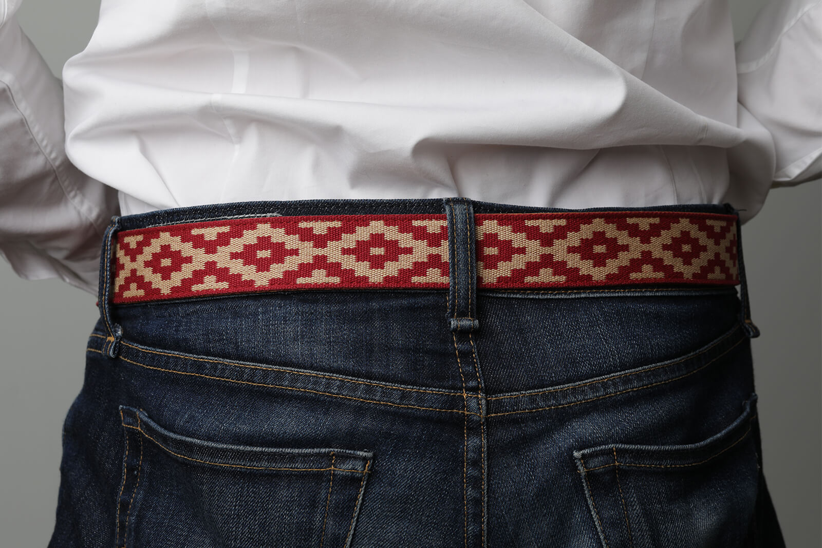 A brown leather belt with a red and beige woven geometric pattern and solid brass buckle.