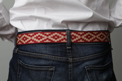 A brown leather belt with a red and beige woven geometric pattern and solid brass buckle.