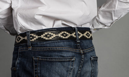 A black leather belt with a white woven geometric pattern and solid brass buckle.