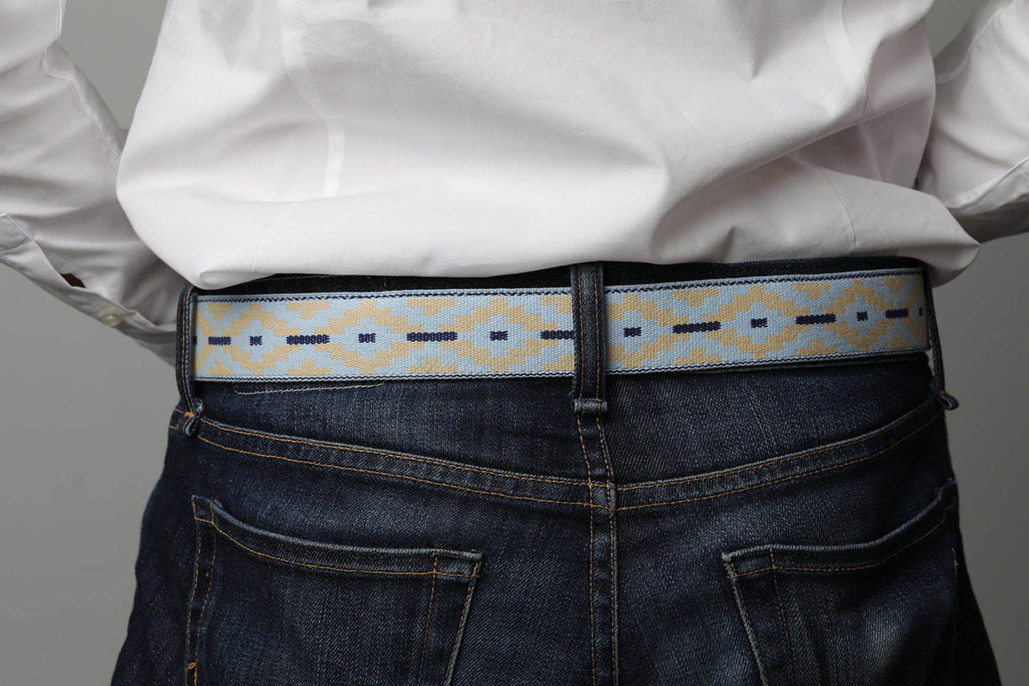 A brown leather belt with a light blue and beige woven pattern and metal nickle buckle.