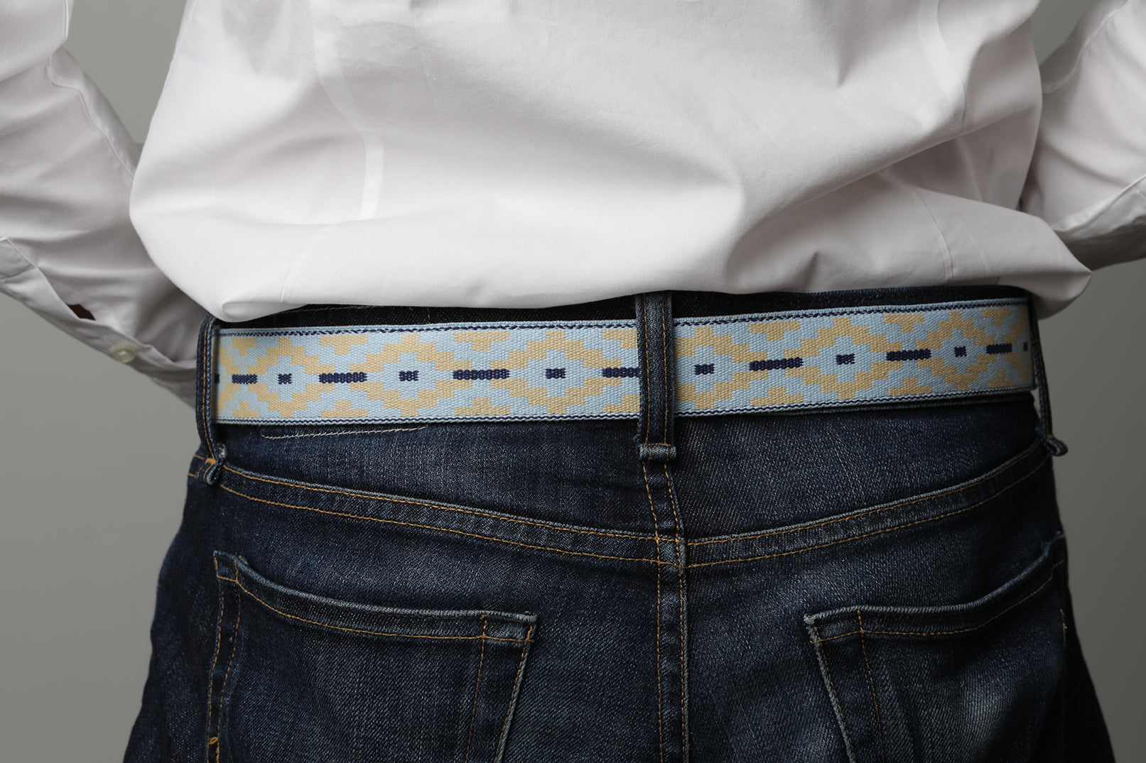 A brown leather belt with a light blue and beige woven pattern and metal nickle buckle.