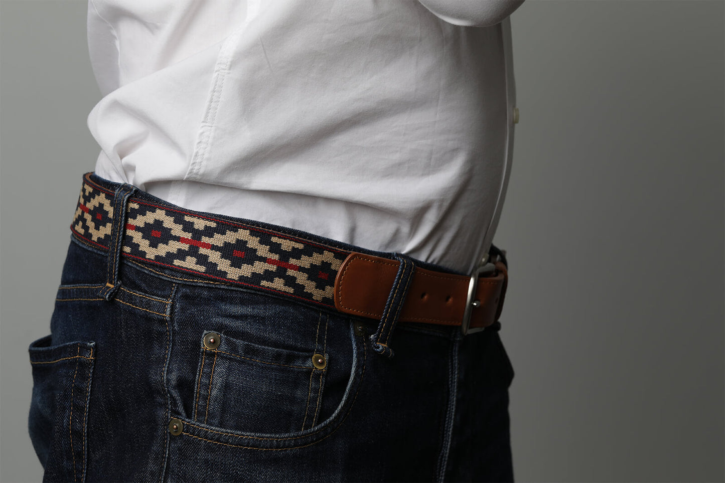 A cognac brown leather belt with a navy, kahki and red woven geometric pattern and solid brass buckle.