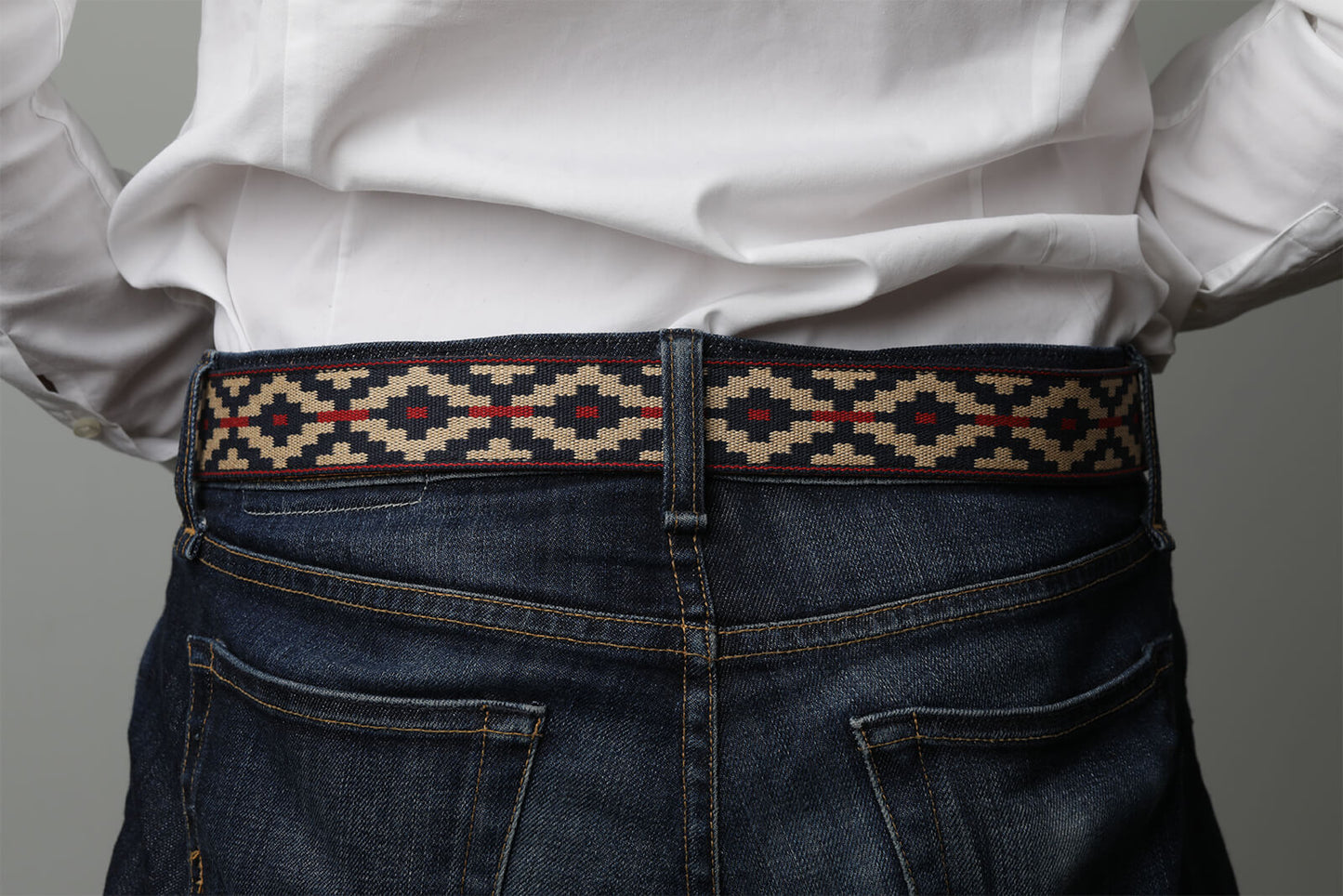 A cognac brown leather belt with a navy, kahki and red woven geometric pattern and solid brass buckle.